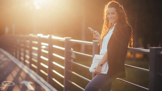 Mulher sorrindo em uma ponte no fim de tarde, com o sol atrás dela
