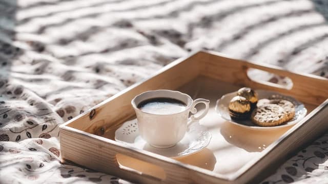 Bandeja com café e biscoitos sobre a cama, luz da manhã