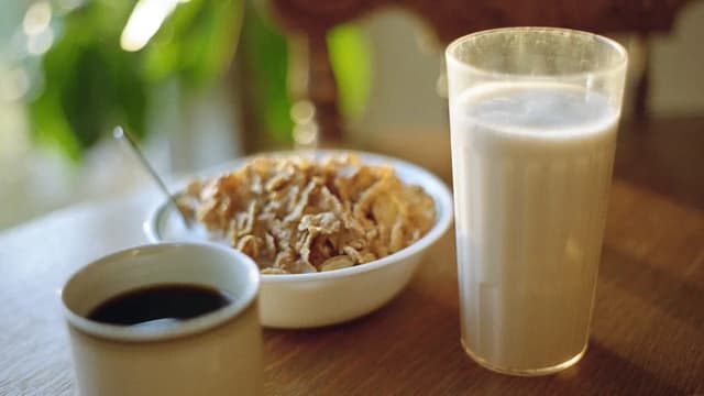 Mesa de café da manhã com xícara de café, tigela de cereal e copo de leite