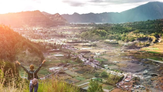 Mulher de braços abertos no alto de uma montanha, olhando o vale ao amanhecer