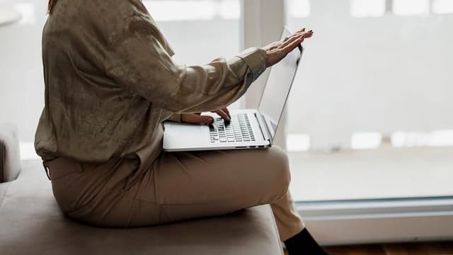 Mulher trabalhando no notebook sentada ao lado de uma janela grande e clara