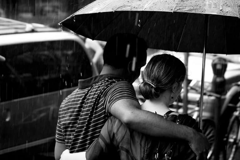 Casal de costas dividindo um guarda-chuva na rua, em preto e branco
