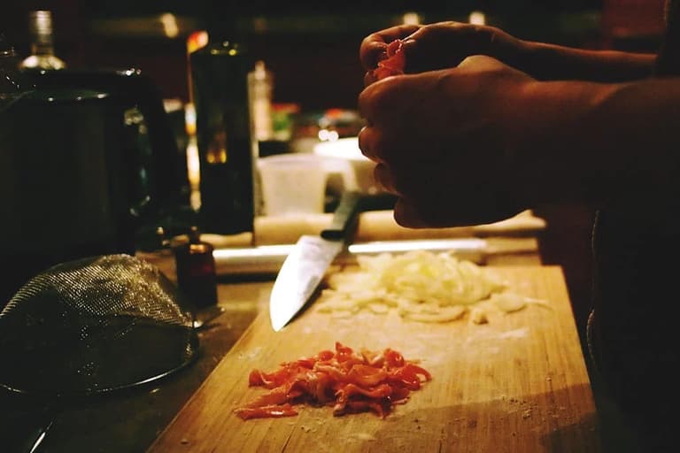 Mãos cortando ingredientes numa tábua de madeira na cozinha, luz baixa