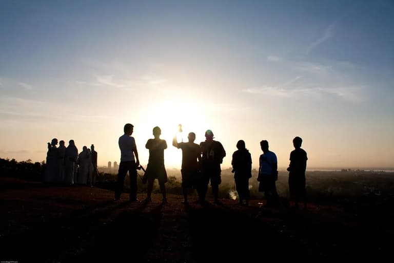 Silhuetas de um grupo de pessoas em uma colina contra o sol nascendo